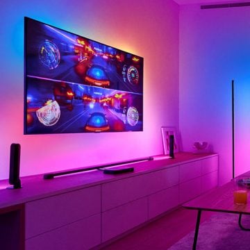 Ein Racing-Game erscheint auf einem großen, an der Wand hängenden Fernsehbildschirm, der von einer synchronisierten Surround-Beleuchtung umgeben ist.