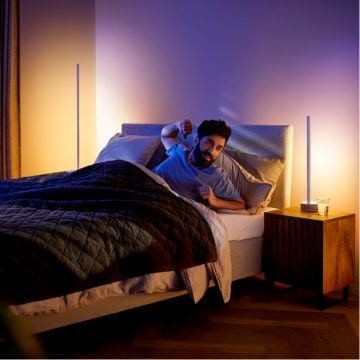 Mann stretcht sich im Bett bei sanft leuchtenden smarten Steh- und Tischlampen 