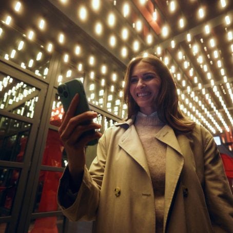 Smiling woman standing under a theater entrance looking at her phone.