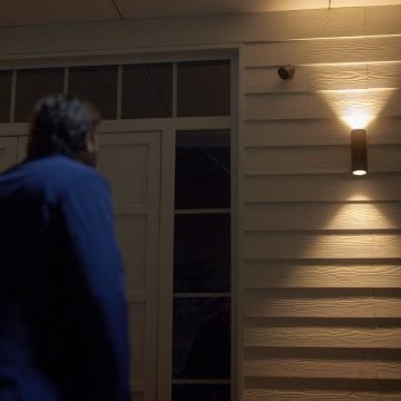Een Philips hue Secure camera aan de muur, gericht op een man buiten een voordeur.